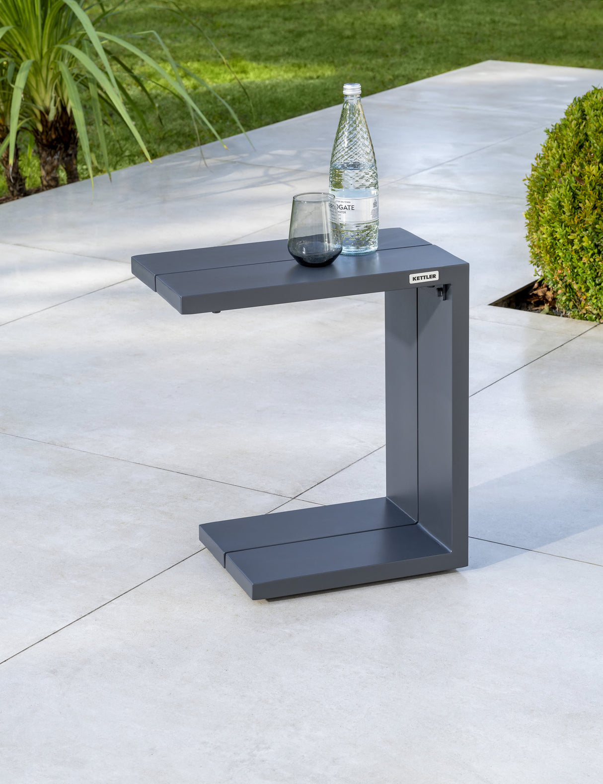 Kettler Elba side table in grey metal, shown in a modern living room setting, perfect for supporting lamps or decorative items.