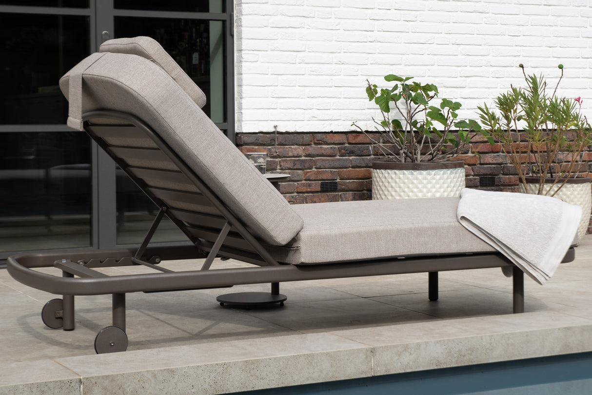 4 Seasons Outdoor Milano Terre sunbed with latte-colored metal frame, cushioned seat, and adjustable headrest for outdoor relaxation.